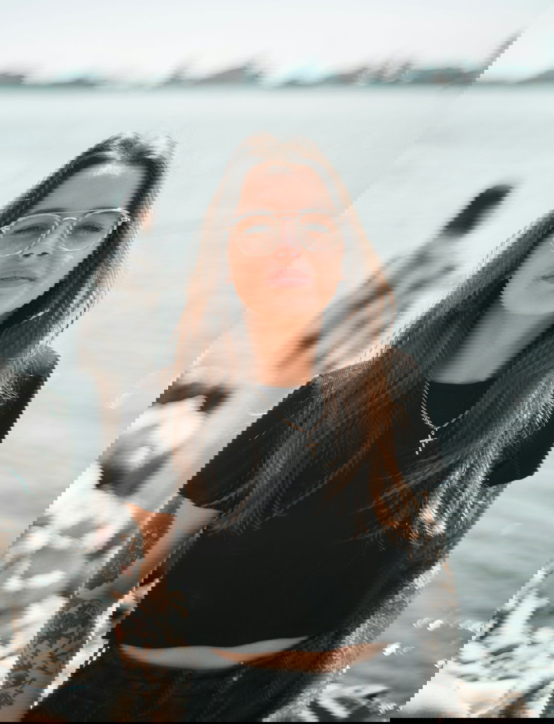 woman in black crew neck t-shirt wearing brown framed eyeglasses standing on rocky shore during